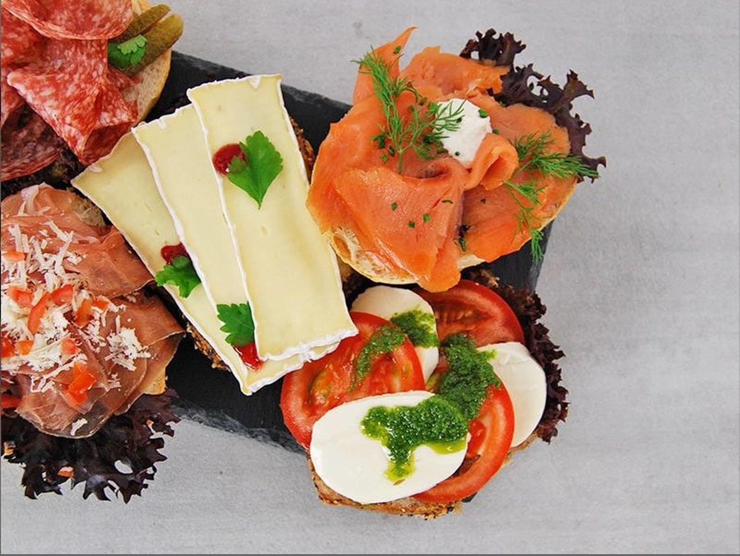 Konditorei Café Gerwig – Eisdiele – Dieses Bild zeigt eine Platte mit verschiedenen belegten Broten oder Vorspeisen, oft auch Tartines oder Canapés genannt.